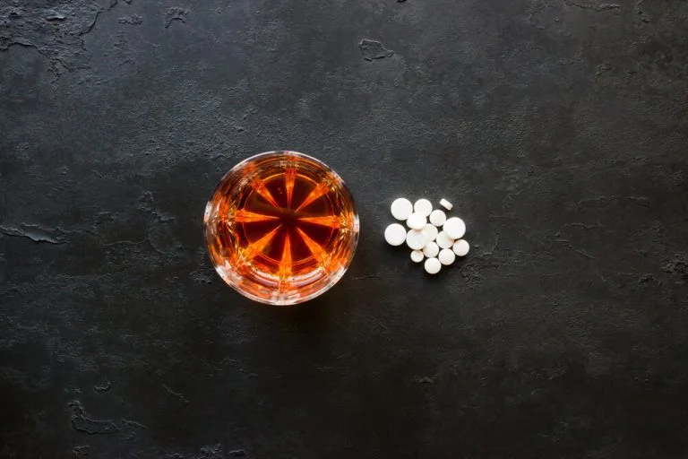 Glass of alcohol with white pills on black surface
