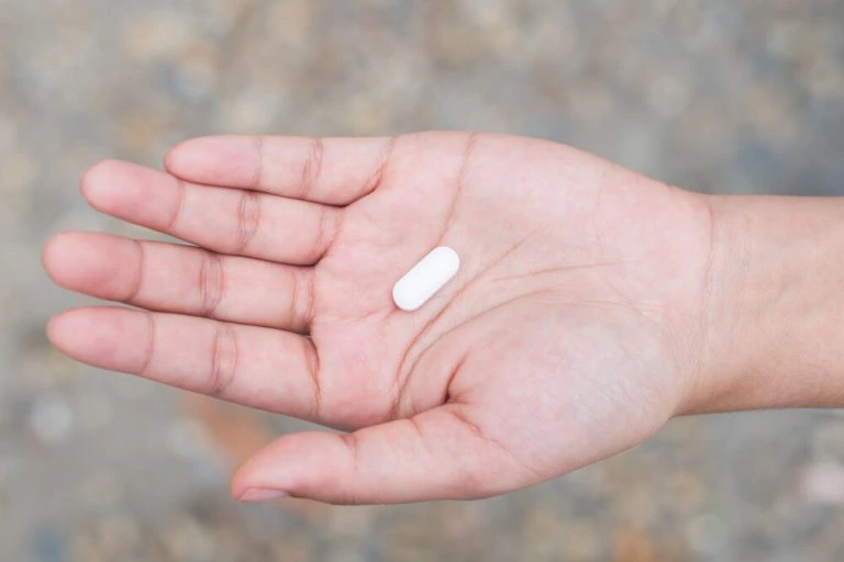 Hand holding single white pill