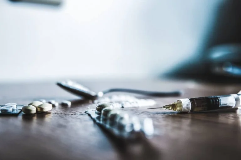 Syringe and pills on wooden surface