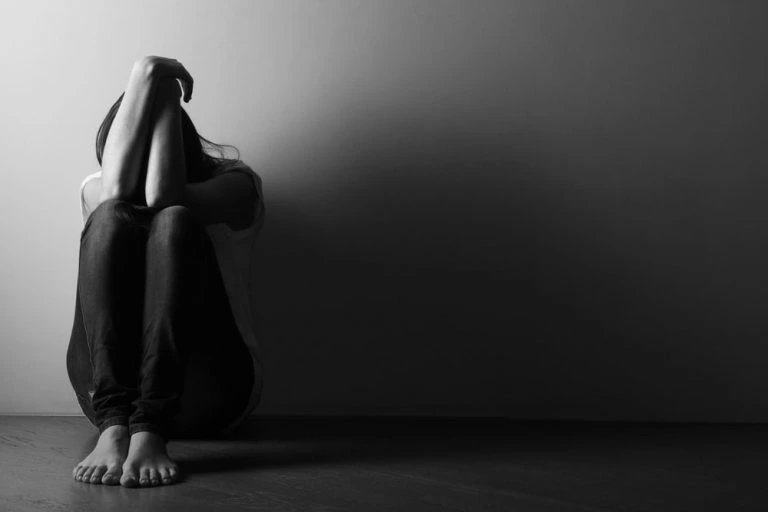 Woman sitting on floor covering face feeling sad